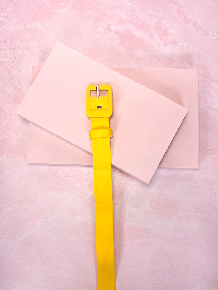 Brighten up your outfit with this yellow sateen belt, a perfect retro-inspired accessory that adds a cheerful pop of color and a touch of vintage charm to any look.