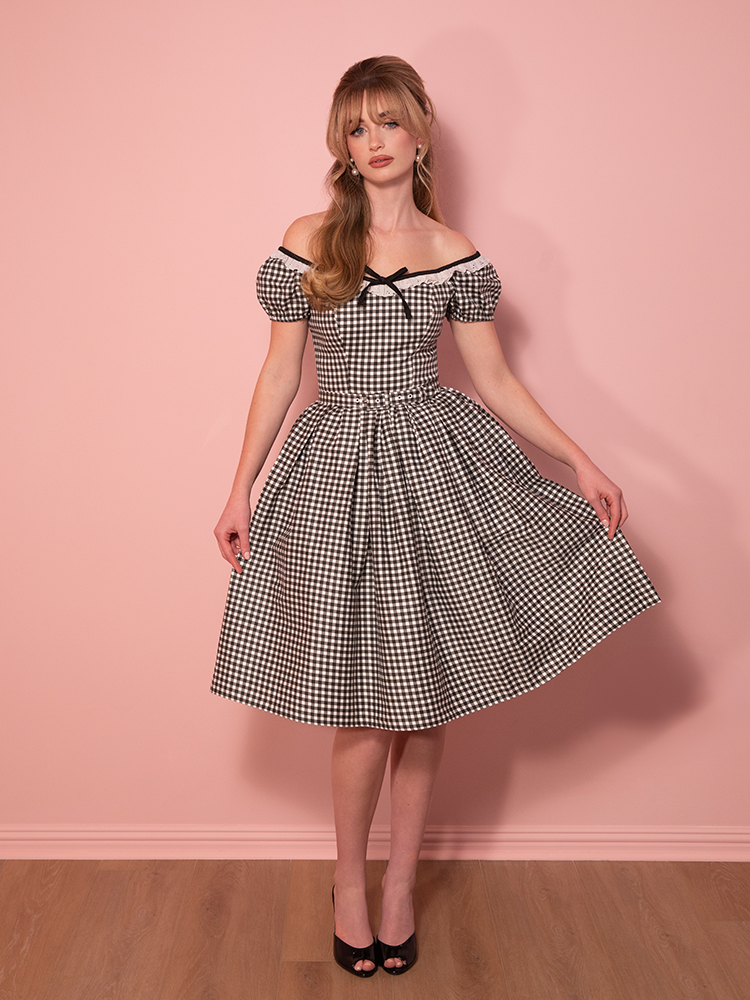 Channel vintage bombshell vibes, with this off-the-shoulder black gingham dress, featuring a structured bodice and voluminous skirt for a pin-up perfect look.
