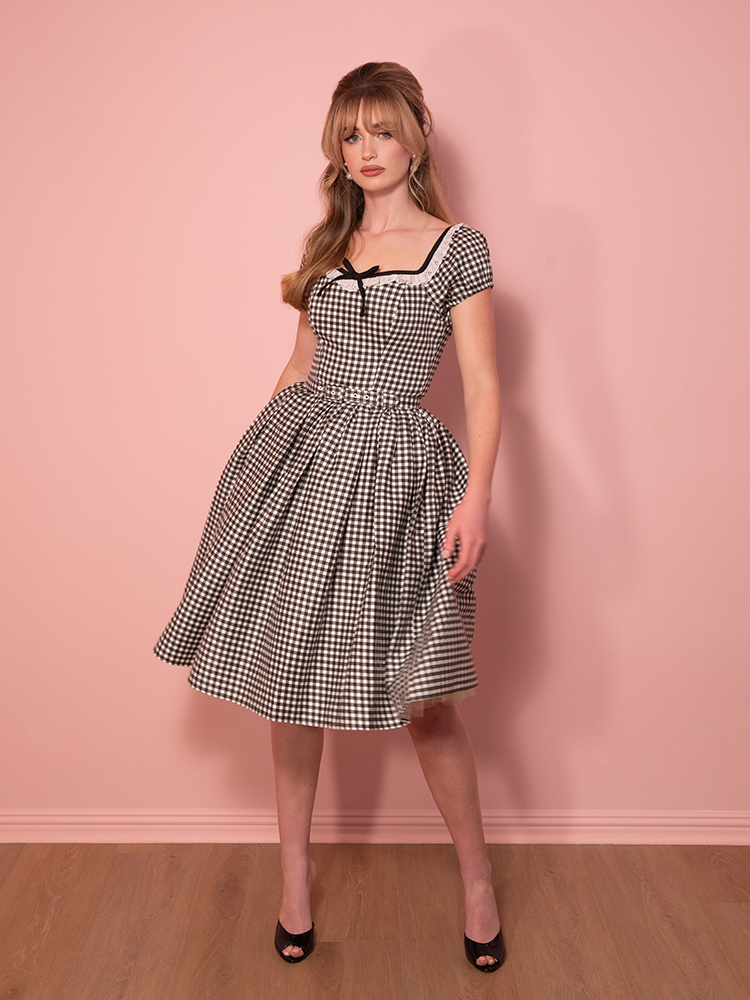 A dreamy nod to 1950s fashion, this Bardot swing dress in black gingham creates a romantic silhouette with its off-the-shoulder neckline and classic flare.
