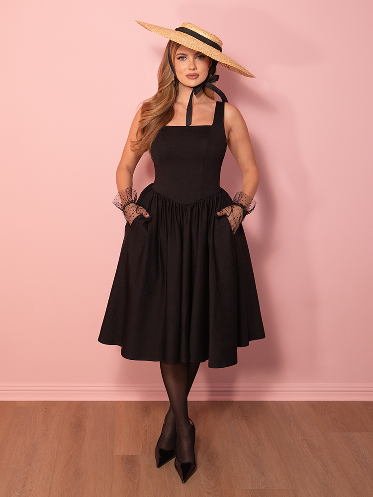 A true vintage bombshell moment, this black swing dress stuns with its sophisticated neckline, nipped-in waist, and voluminous skirt for a show-stopping look.
