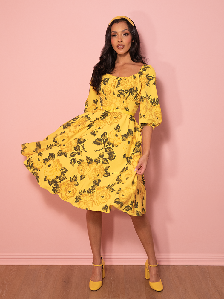 A nod to classic femininity, this vintage rose-print vacation dress in yellow cinches the waist and flows into a breezy, elegant skirt.
