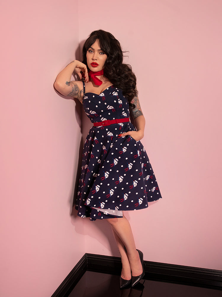 Leaning in the corner of the room, Micheline Pitt models the latest retro style dress from Vixen Clothing - GHOSTBUSTERS™ Maneater Swing Dress in Stay Puft Novelty Print.