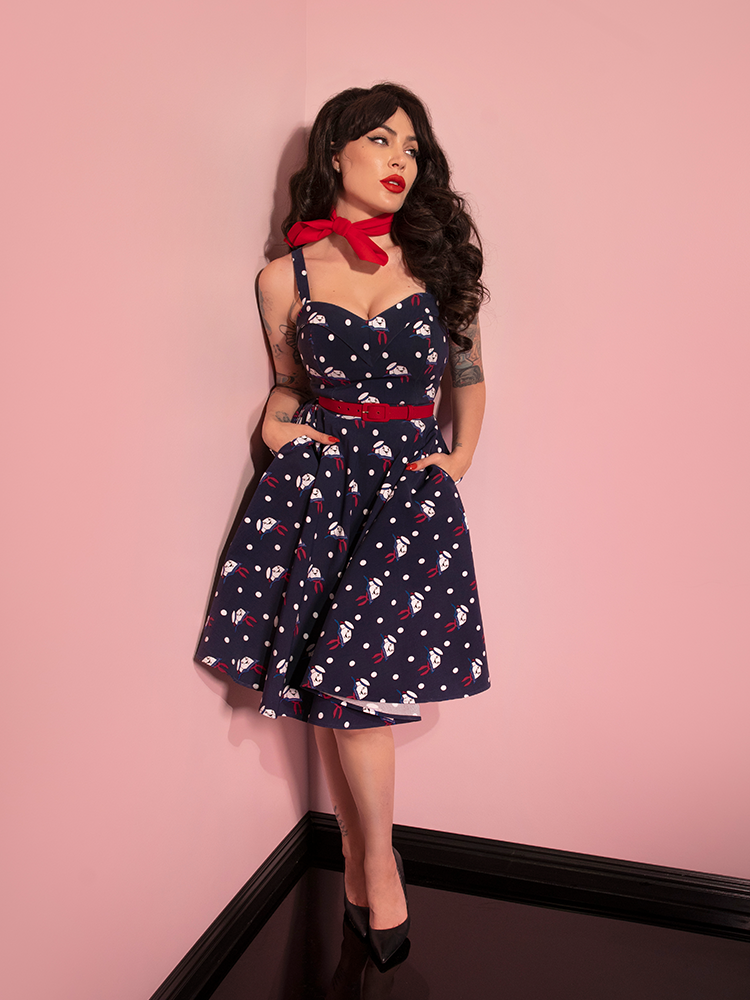 Full length shot of Micheline Pitt standing in the corner of an all pink room while wearing the GHOSTBUSTERS™ Maneater Swing Dress in Stay Puft Novelty Print. 