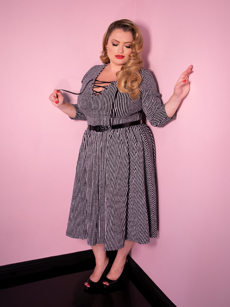 Blondie looking down while modeling the Vixen Clothing Miss Kitty swing dress in black stripes.