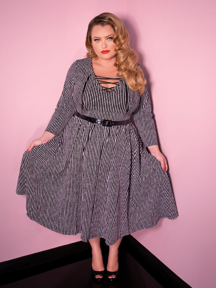 Blondie looking at the camera while holding her skirt modeling the Vixen Clothing Miss Kitty swing dress in black stripes.