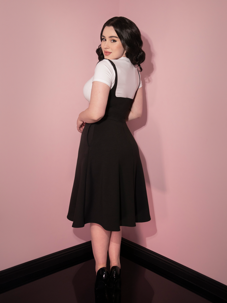 Rachel Sedory with her body turned away but looking back at the camera, shows off the Cozy Skater Skirt Jumper in Black from retro clothing company Vixen Clothing.